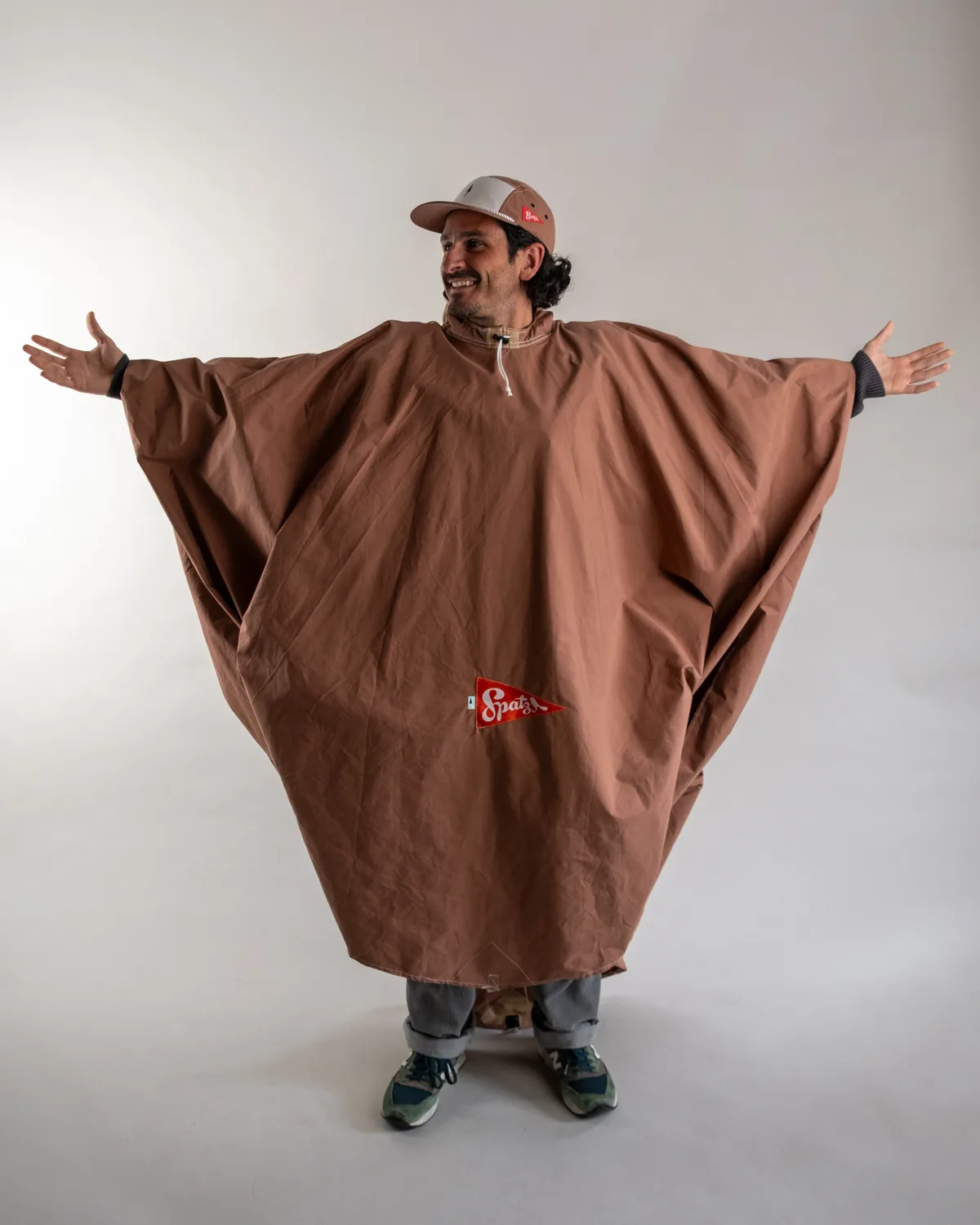 Ein grinsender Mann in einem rostbraunen Poncho.